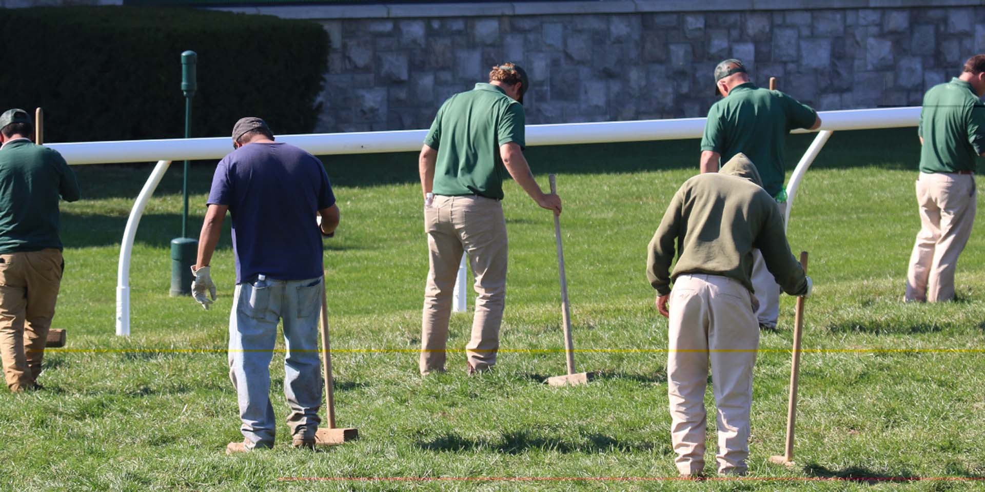 An action shot of Keeneland team members tamping down turf divots.